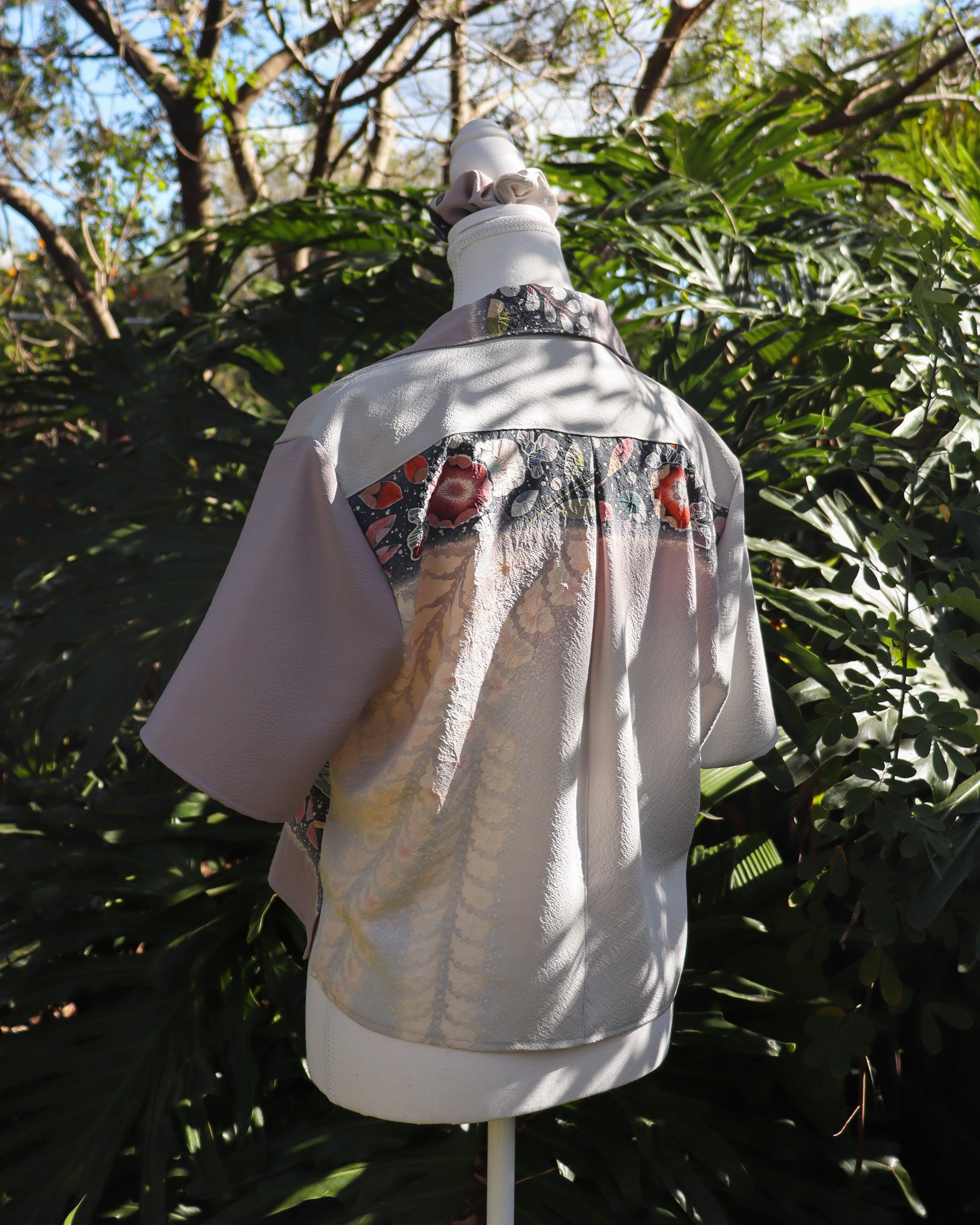 A mannequin wearing a silk shirt with floral patterns in a forest setting