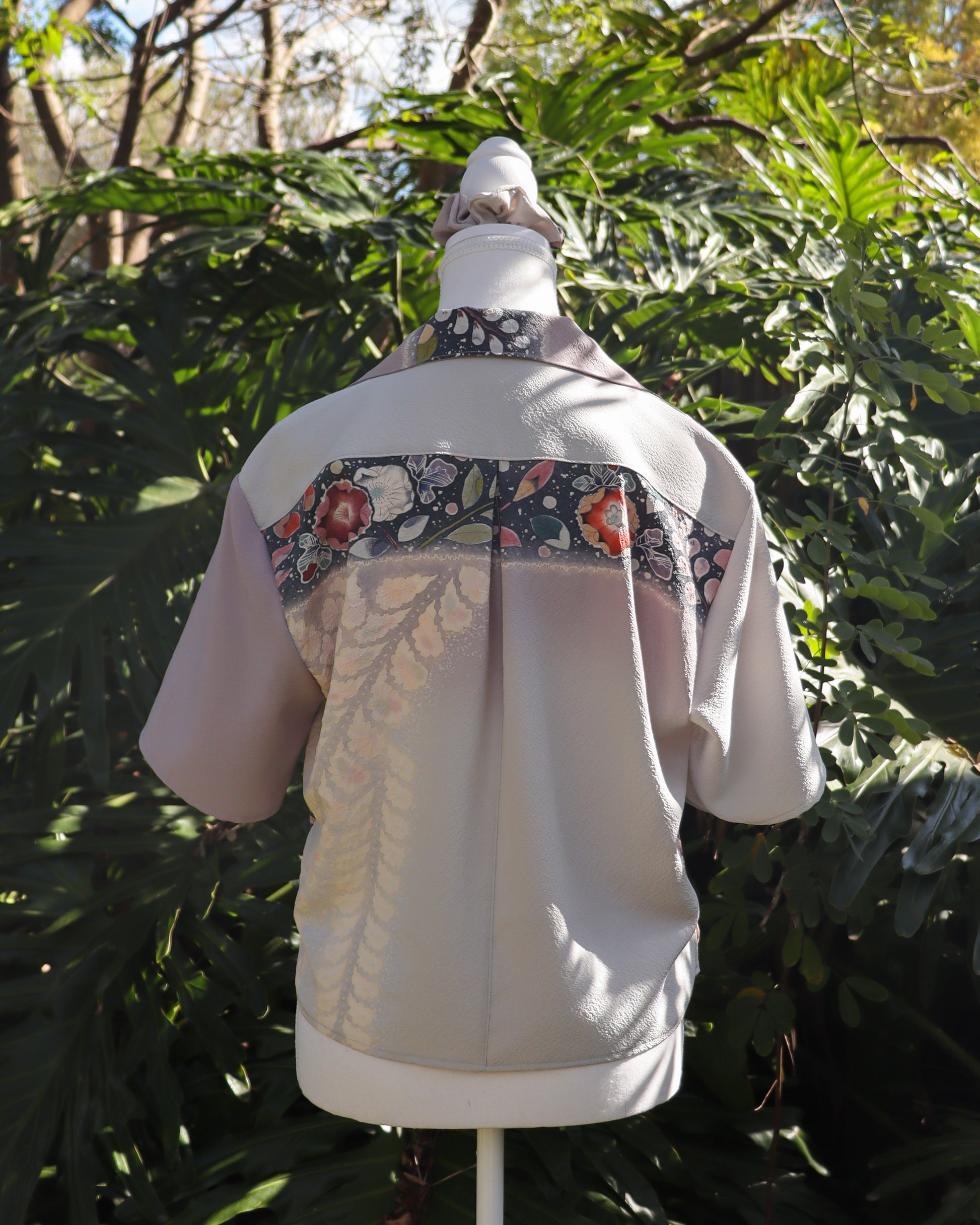 White shirt with floral patterns on a mannequin against a green leafy background