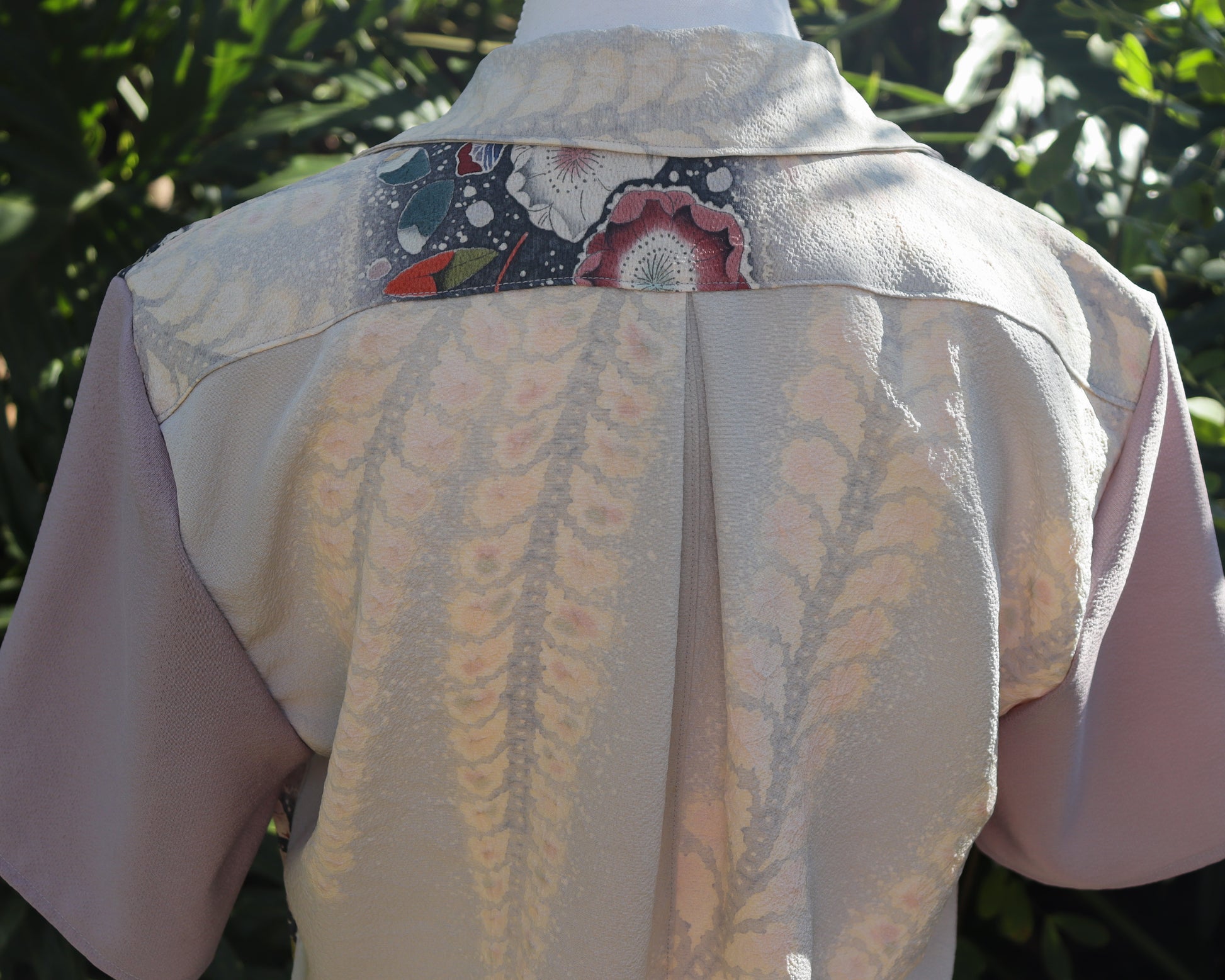 Back view of a light-colored shirt with a patterned patch on a blurred green background