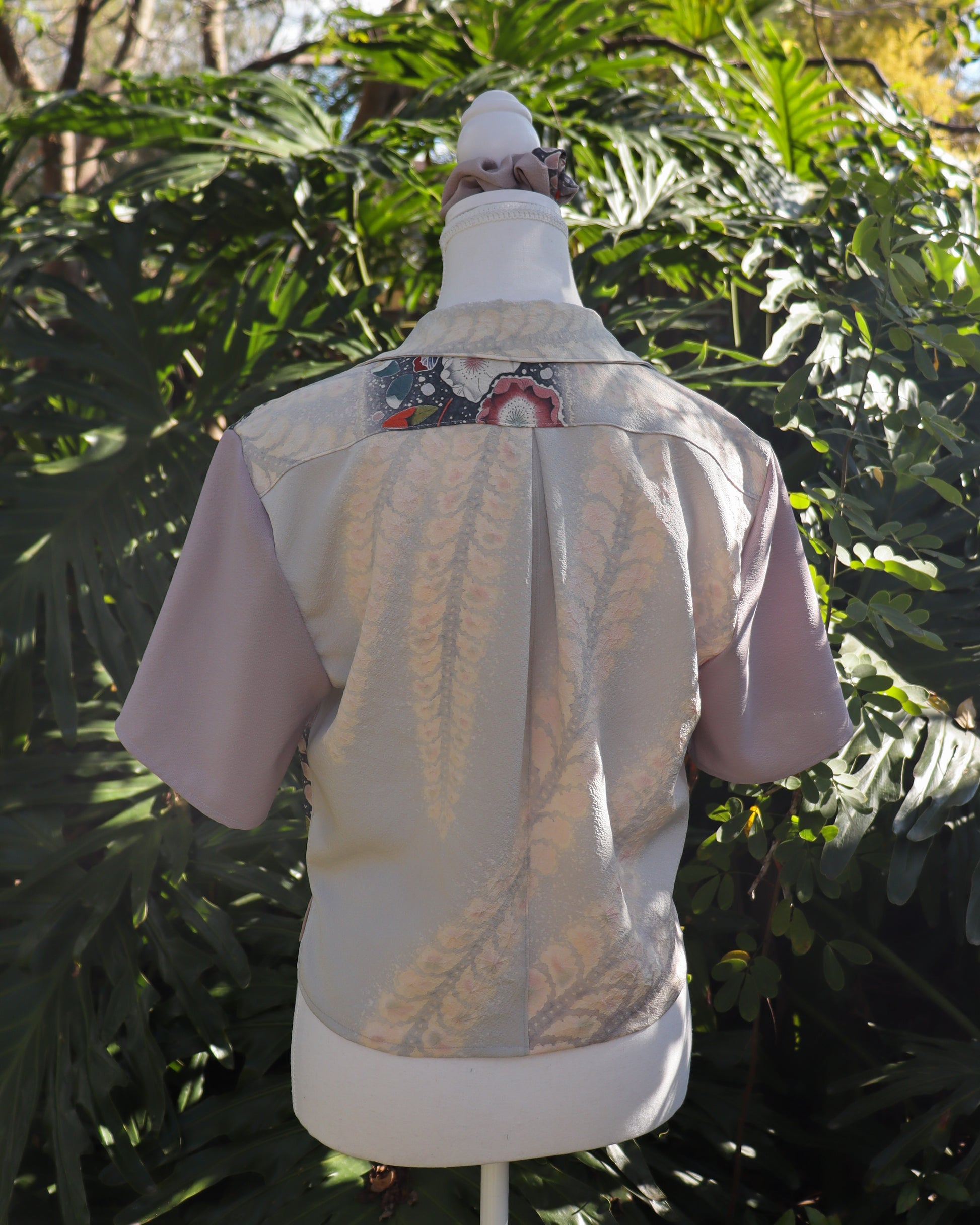 Mannequin wearing a silk shirt with floral pattern, set against a green leafy background.