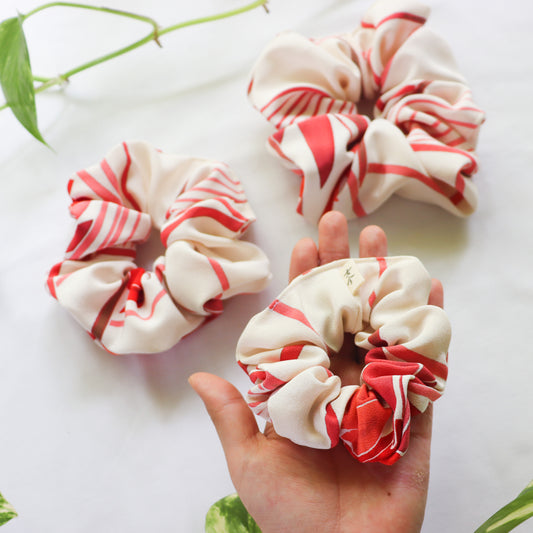 Red and white striped scrunchies on a white surface with a hand holding one.