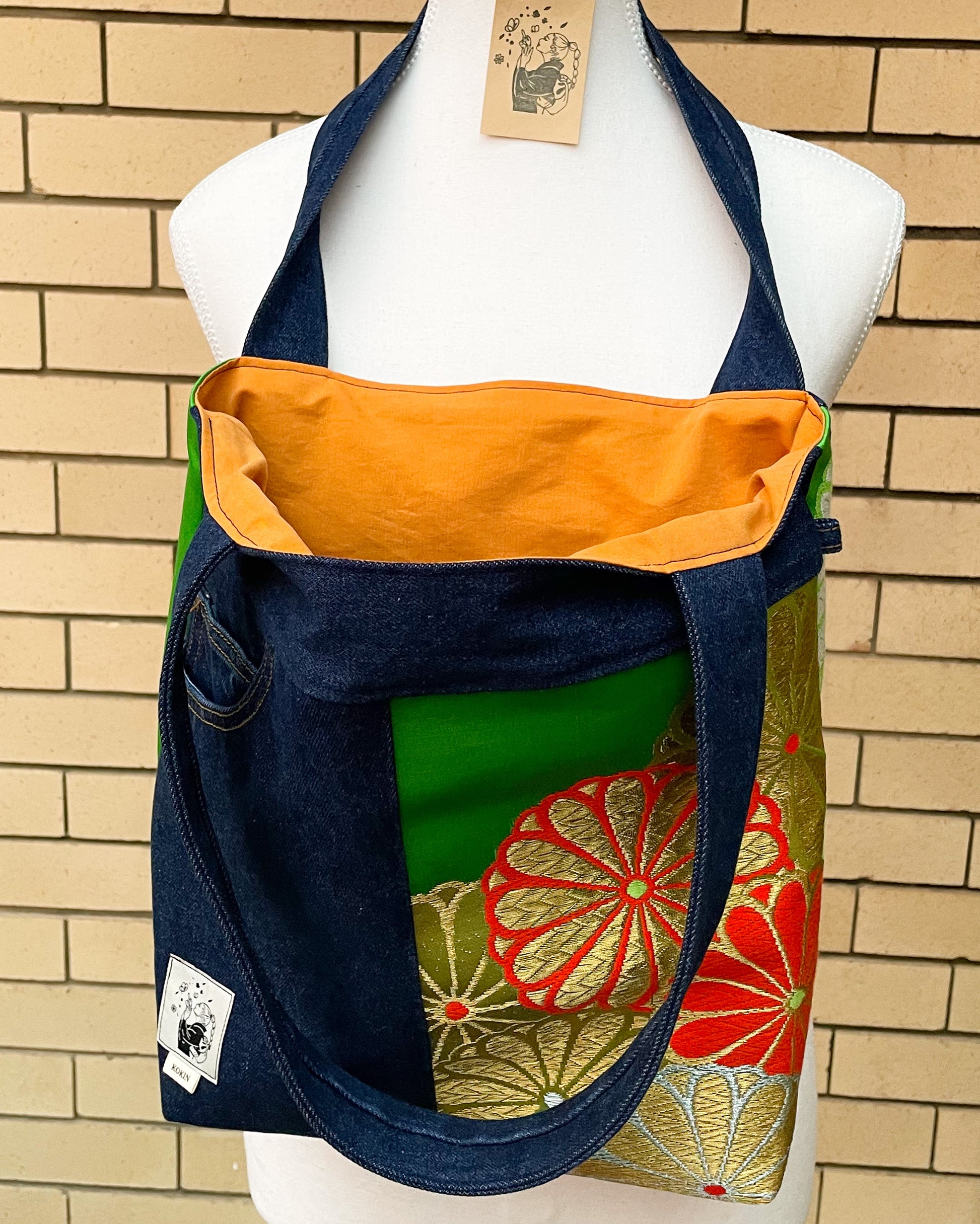 Colorful tote bag with floral patterns on a mannequin against a brick wall.
