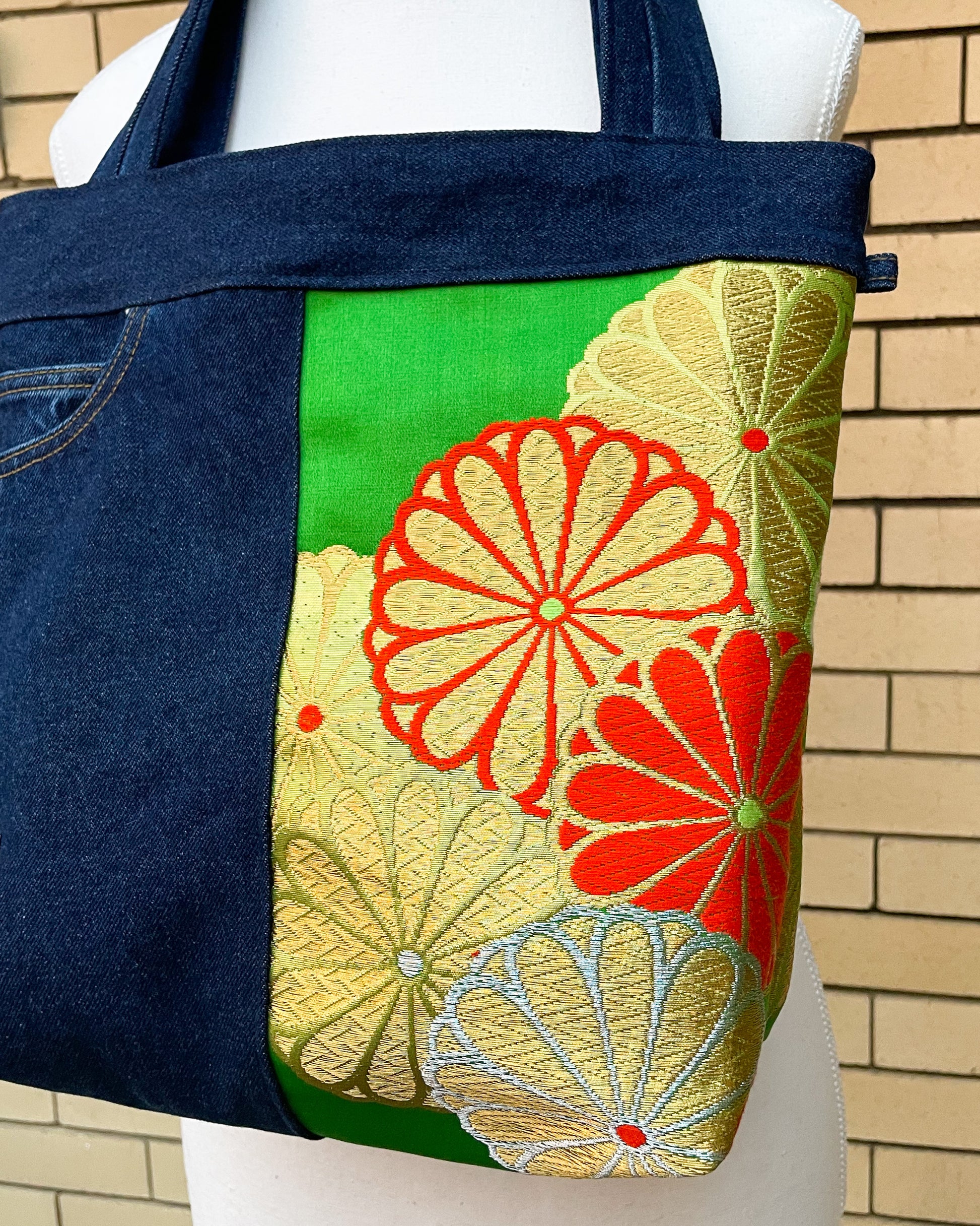 Tote bag with floral patterns on a mannequin against a brick wall.