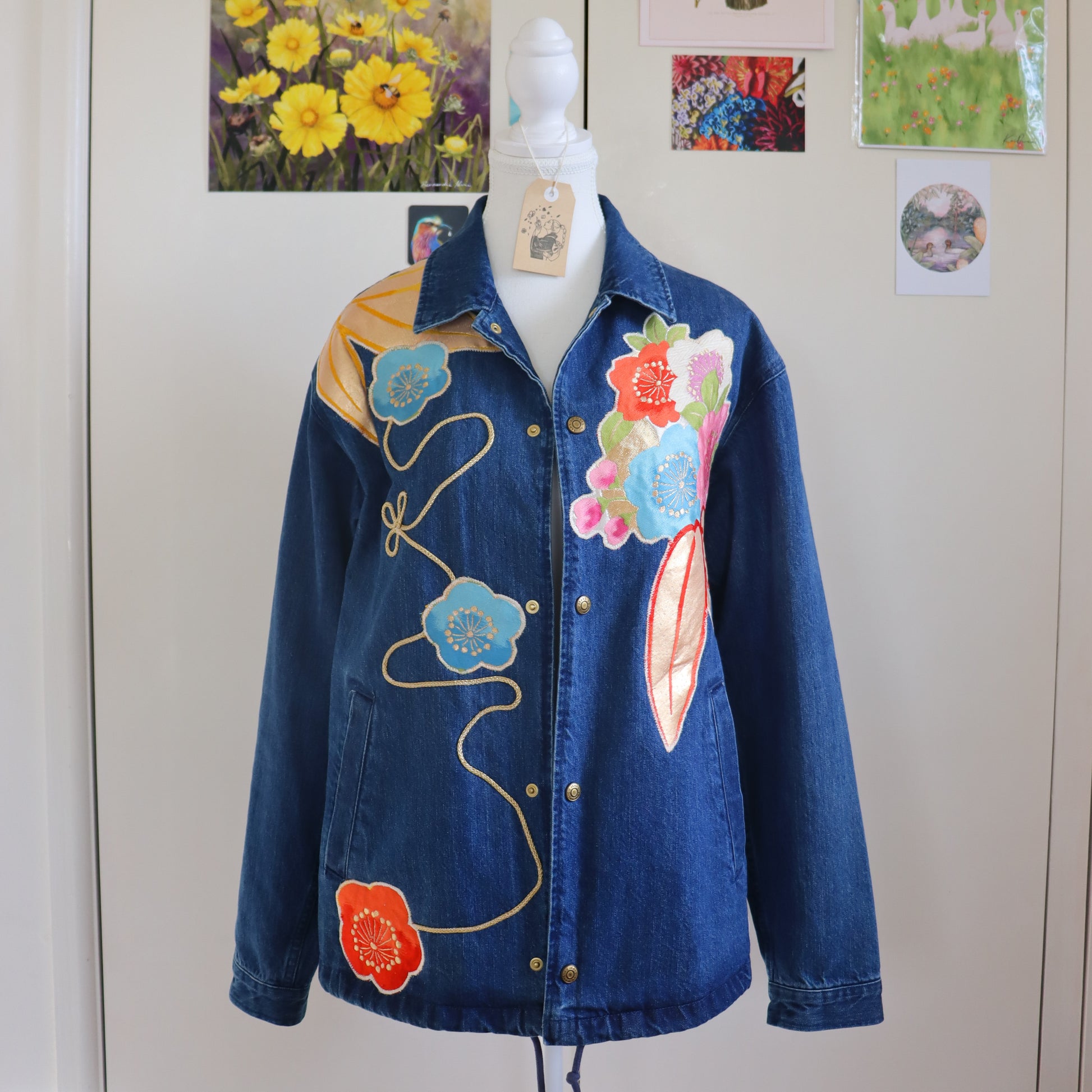 Blue denim jacket with floral embroidery on a mannequin against a wall with floral decorations.