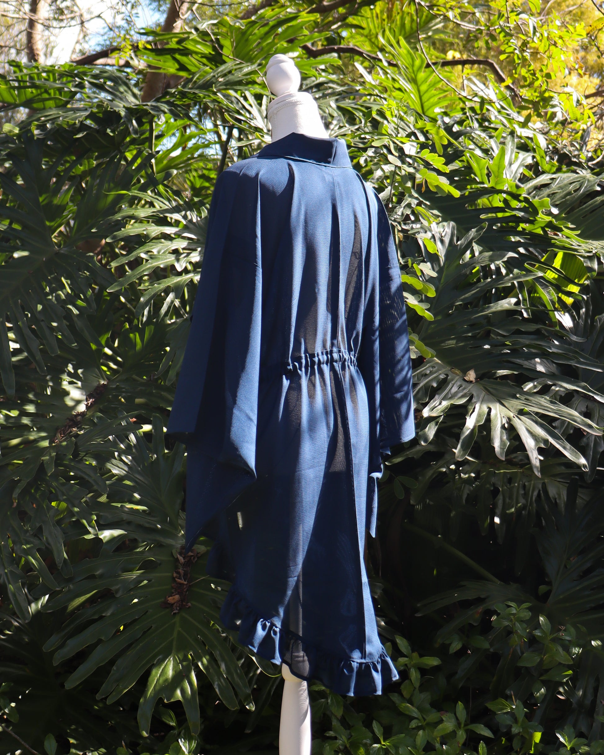 Mannequin wearing a blue kimono cardigan with a natural background of green foliage