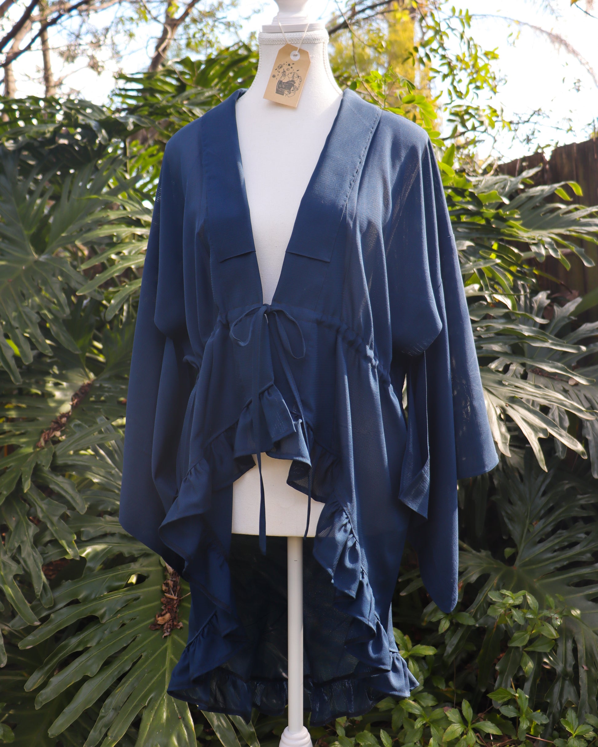 Navy blue kimono-style garment on a mannequin against a green leafy background