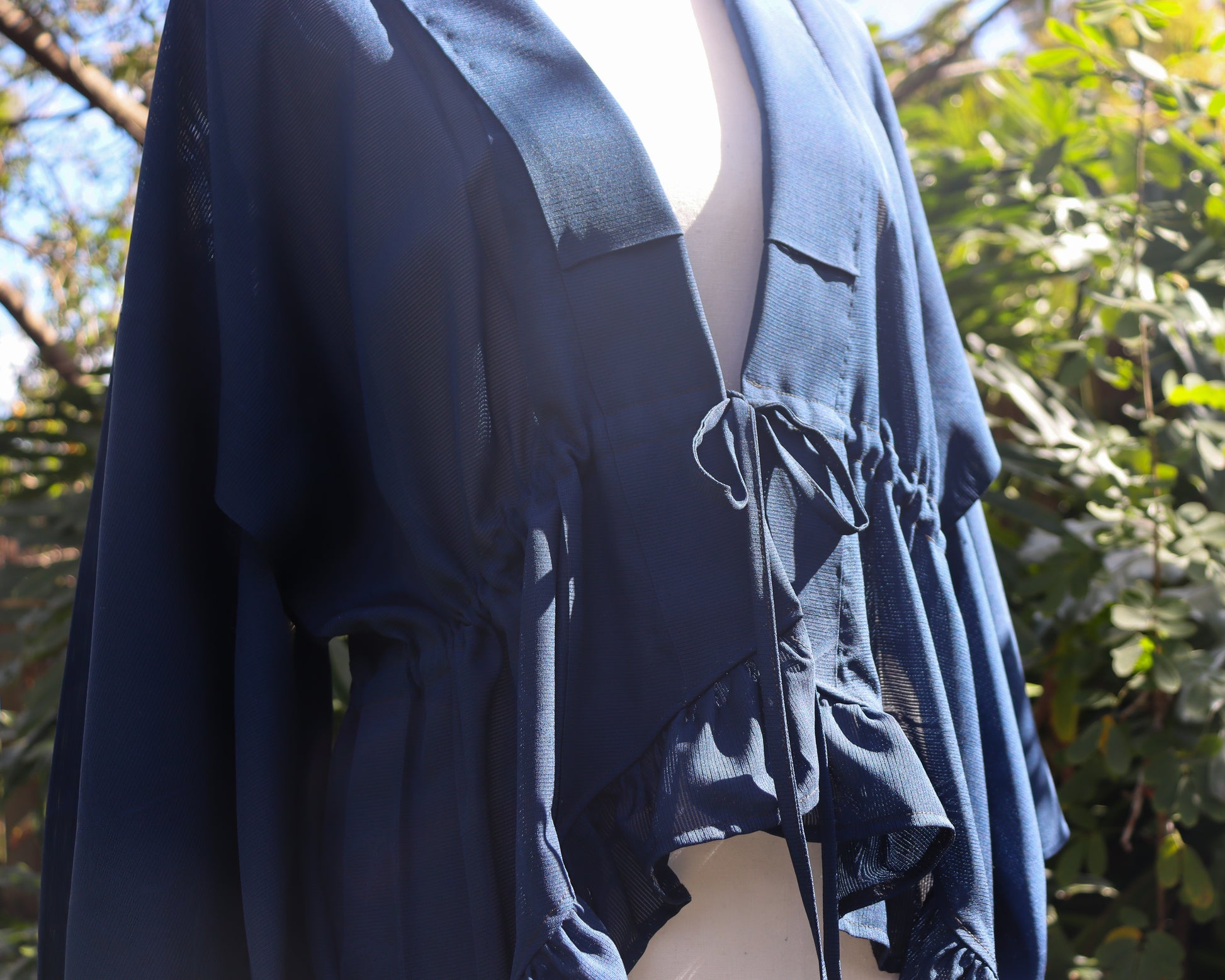 Navy blue dress with ruffled details against a blurred natural background