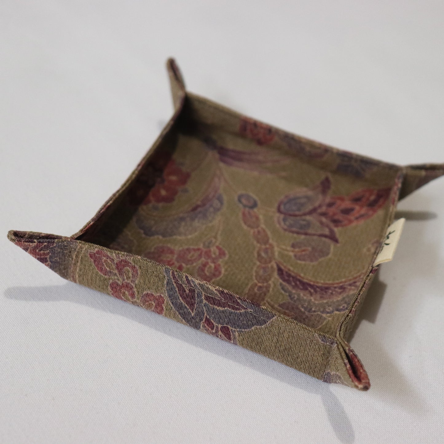 A closeup photo of a fabric tray in brown fabric with floral pattern in a white background.