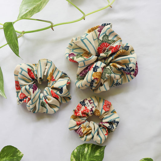 Three colorful scrunchies on a white surface with green leaves.
