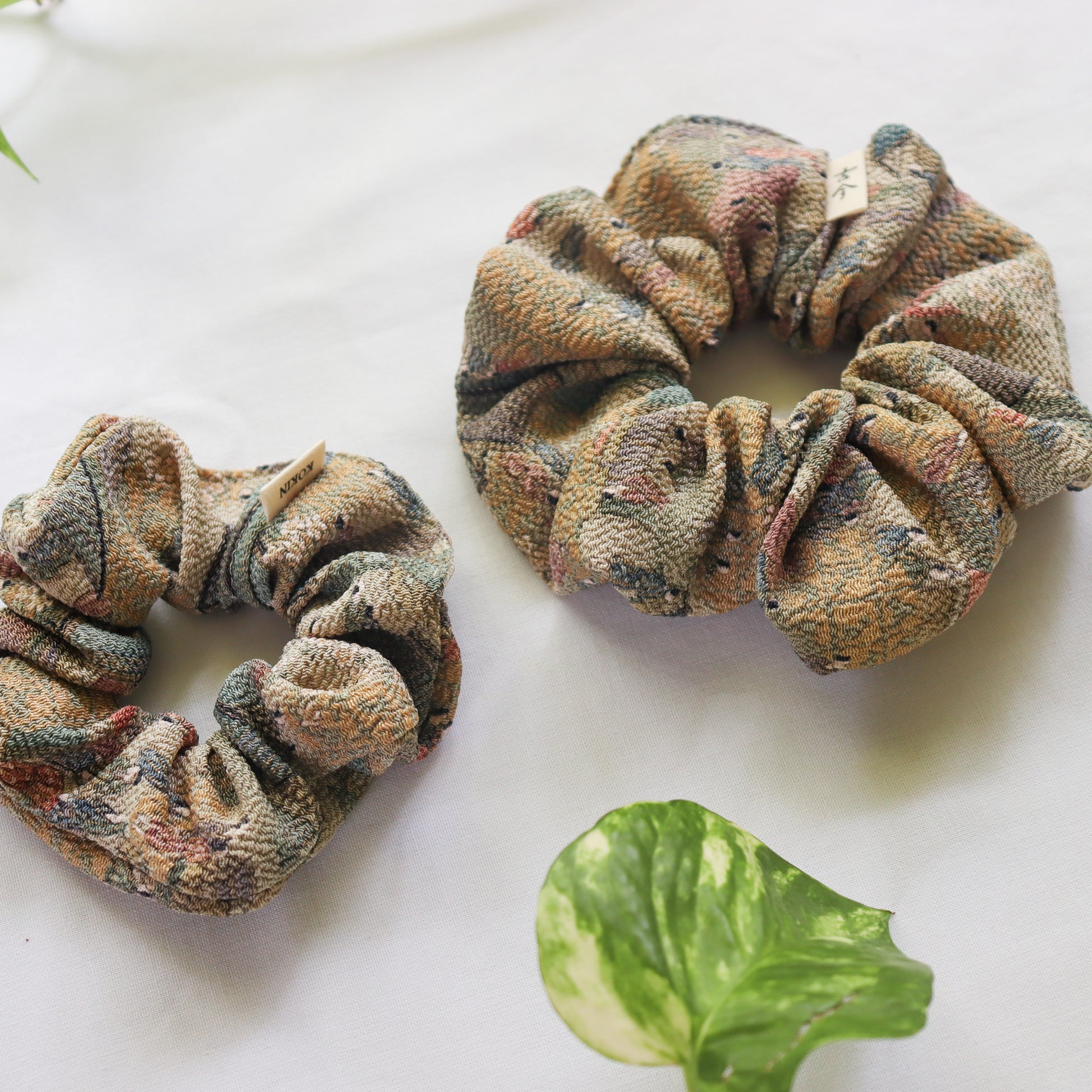 Two patterned scrunchies on a white surface with green leaves.