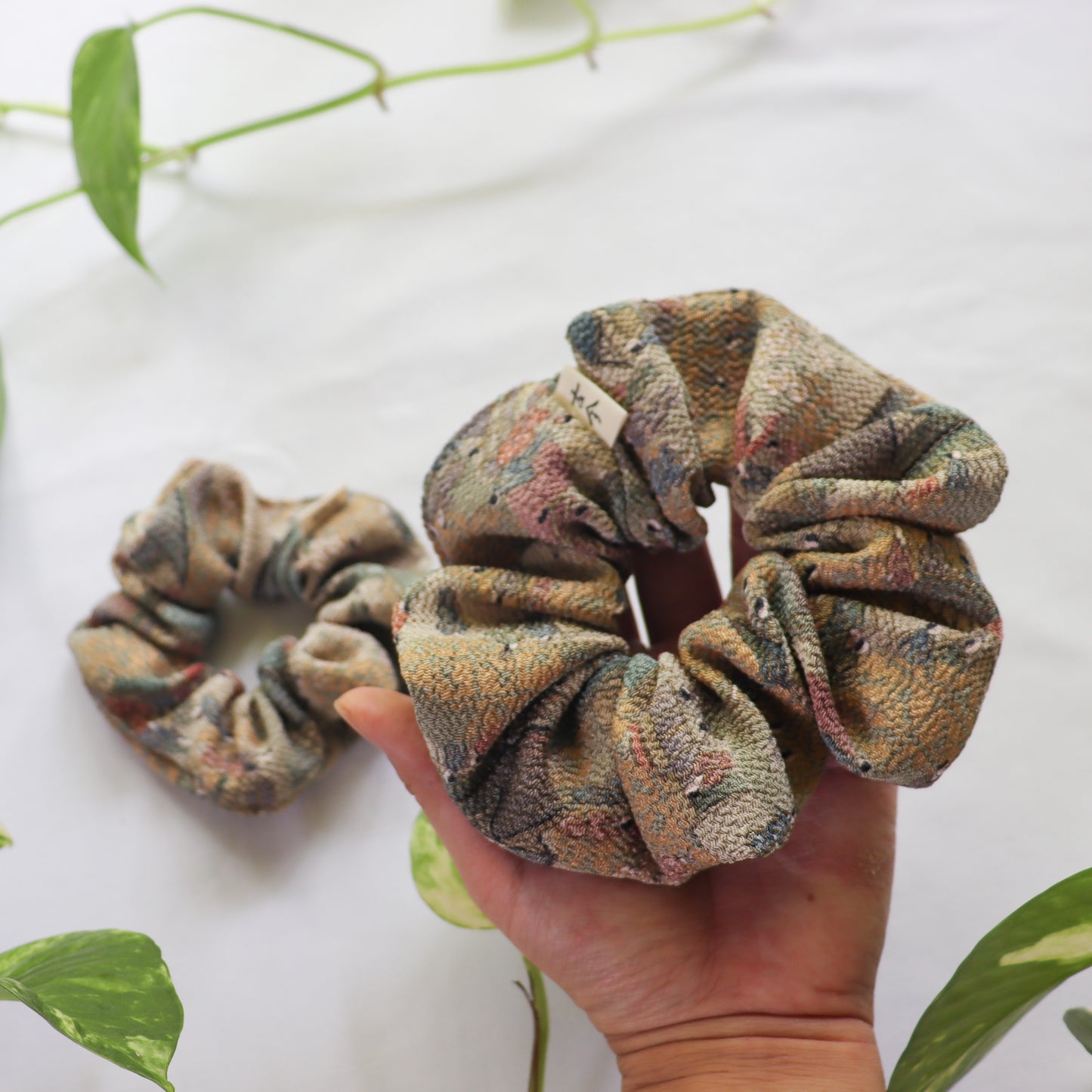 Hand holding a patterned scrunchie with a white background and green leaves.