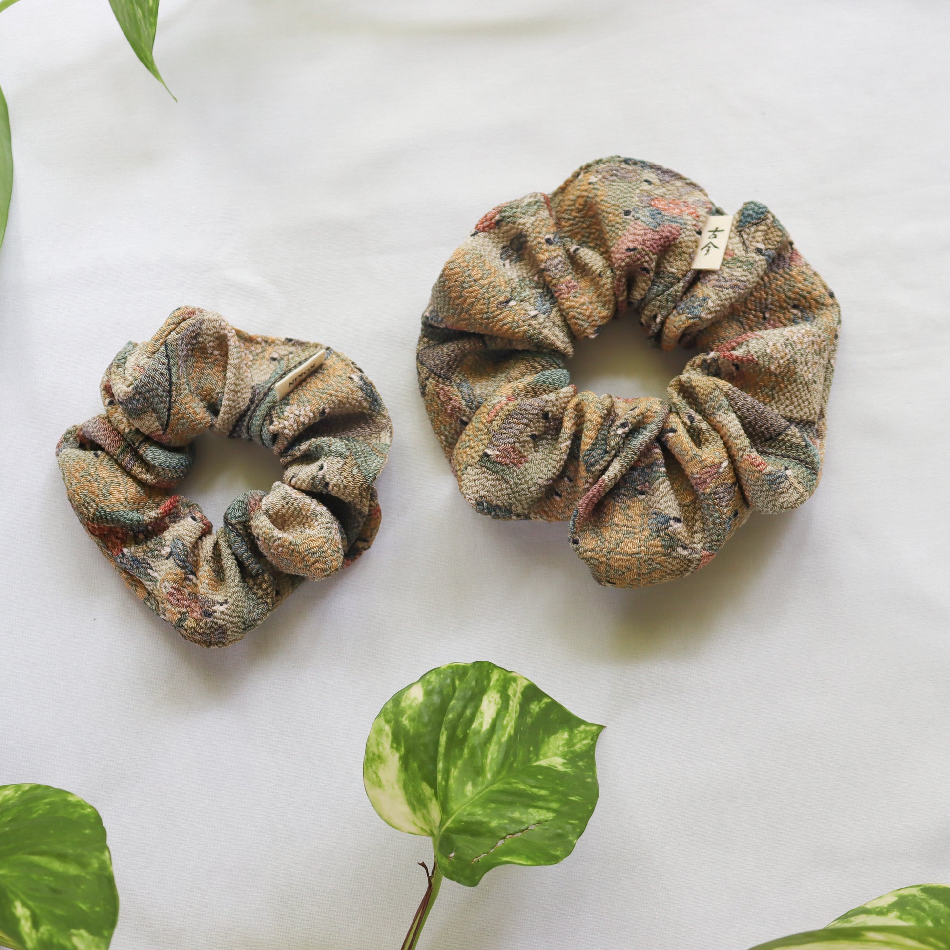 Two patterned scrunchies on a white surface with green leaves.