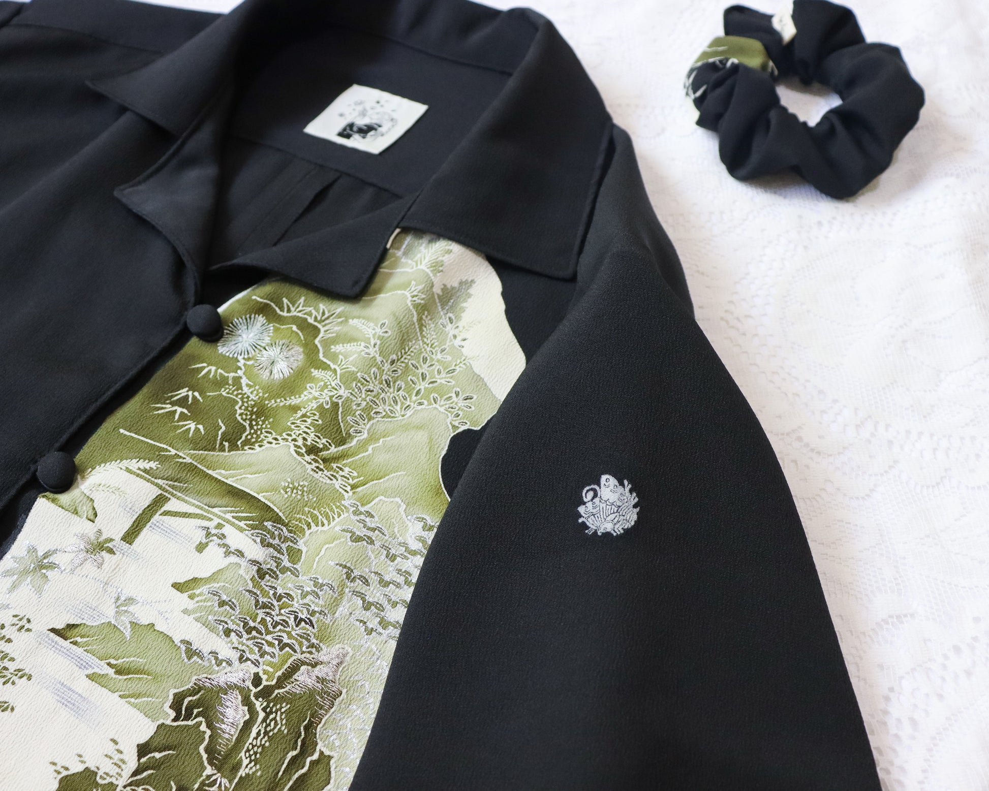 Black blazer with floral pattern and white emblem on a white surface