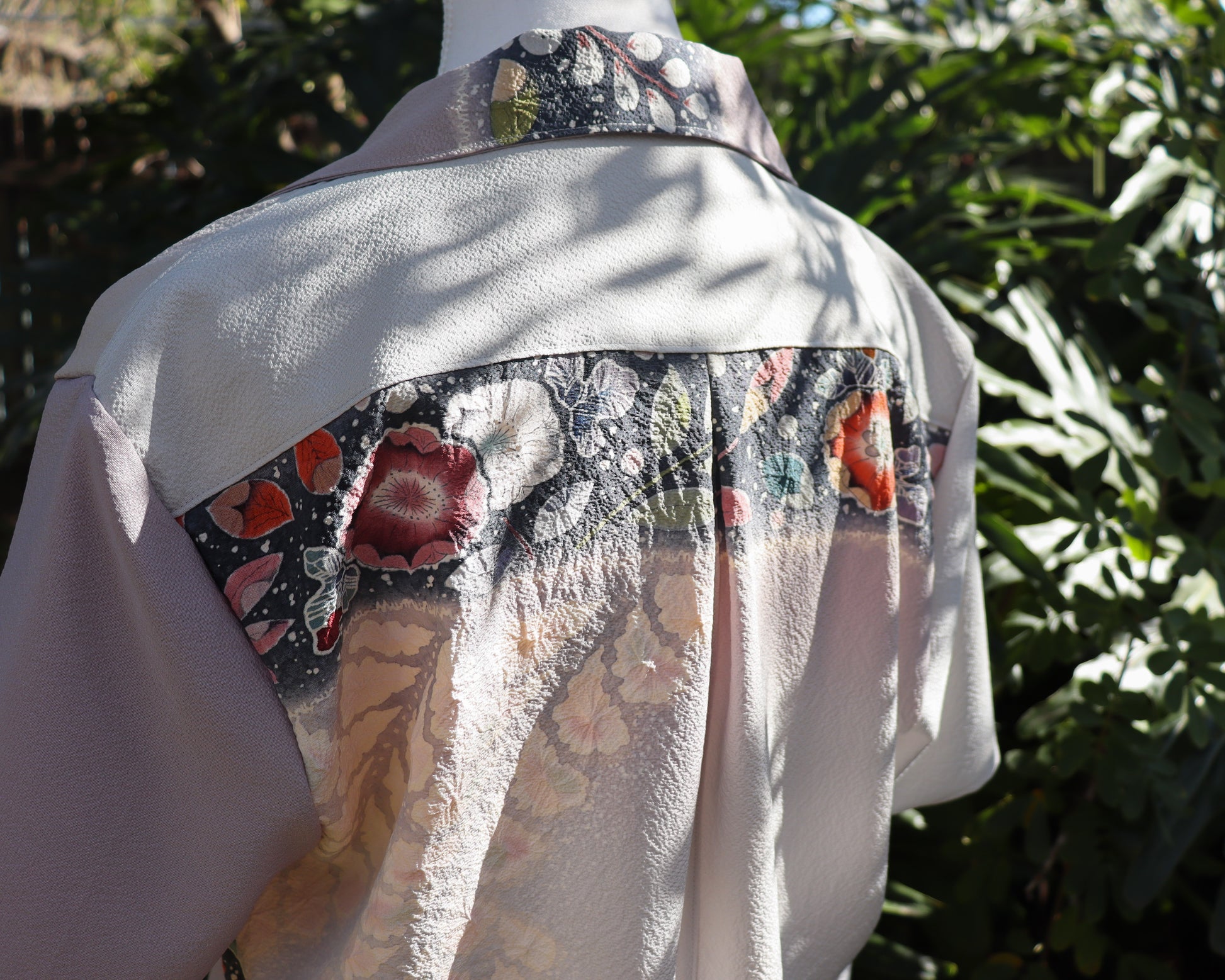 Light-colored garment with floral pattern on a mannequin against a green leafy background