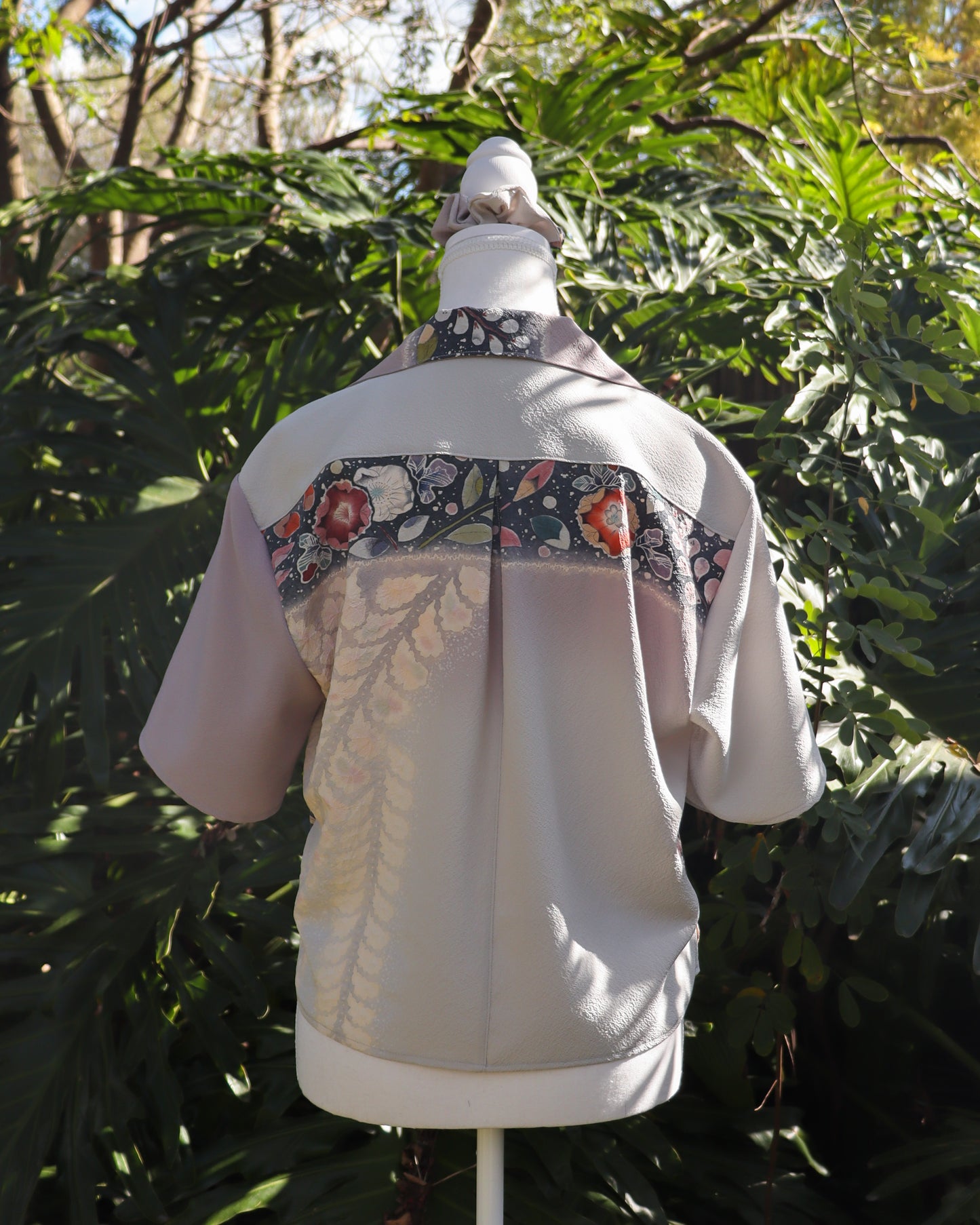 White shirt with floral patterns on a mannequin against a green leafy background