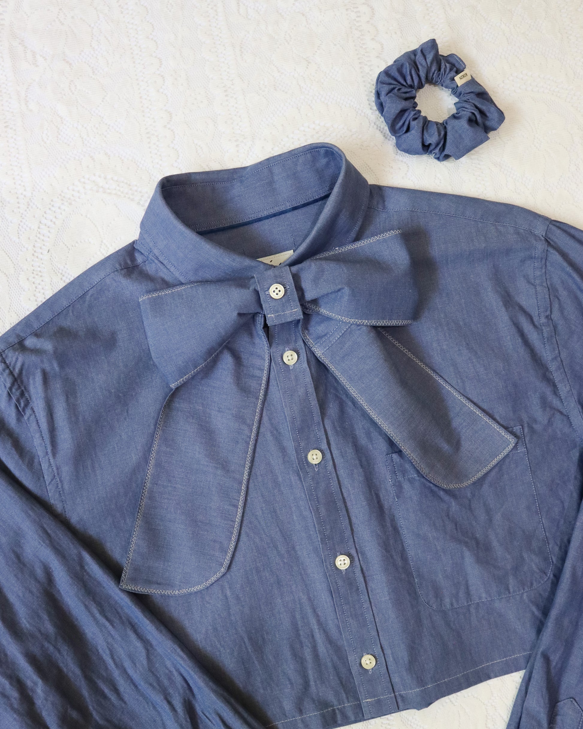 Blue shirt with a bow collar and matching scrunchie on a white background
