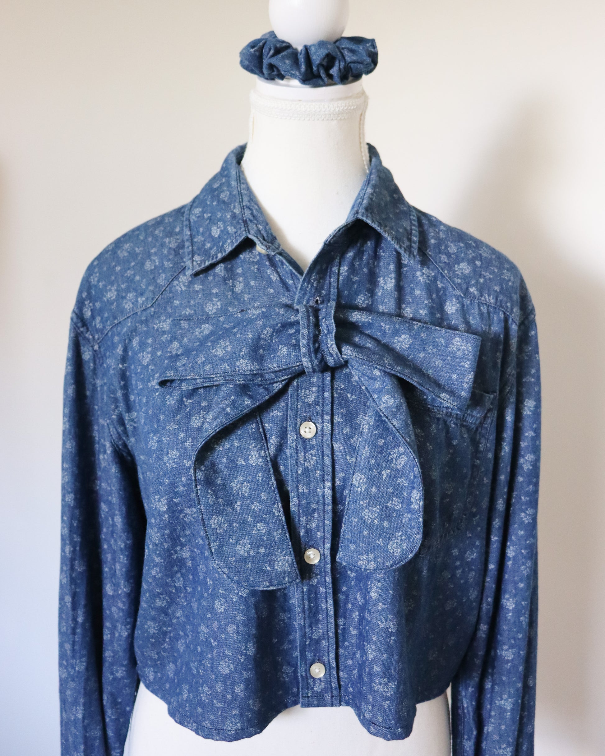 Blue denim shirt with floral pattern on a mannequin against a white background