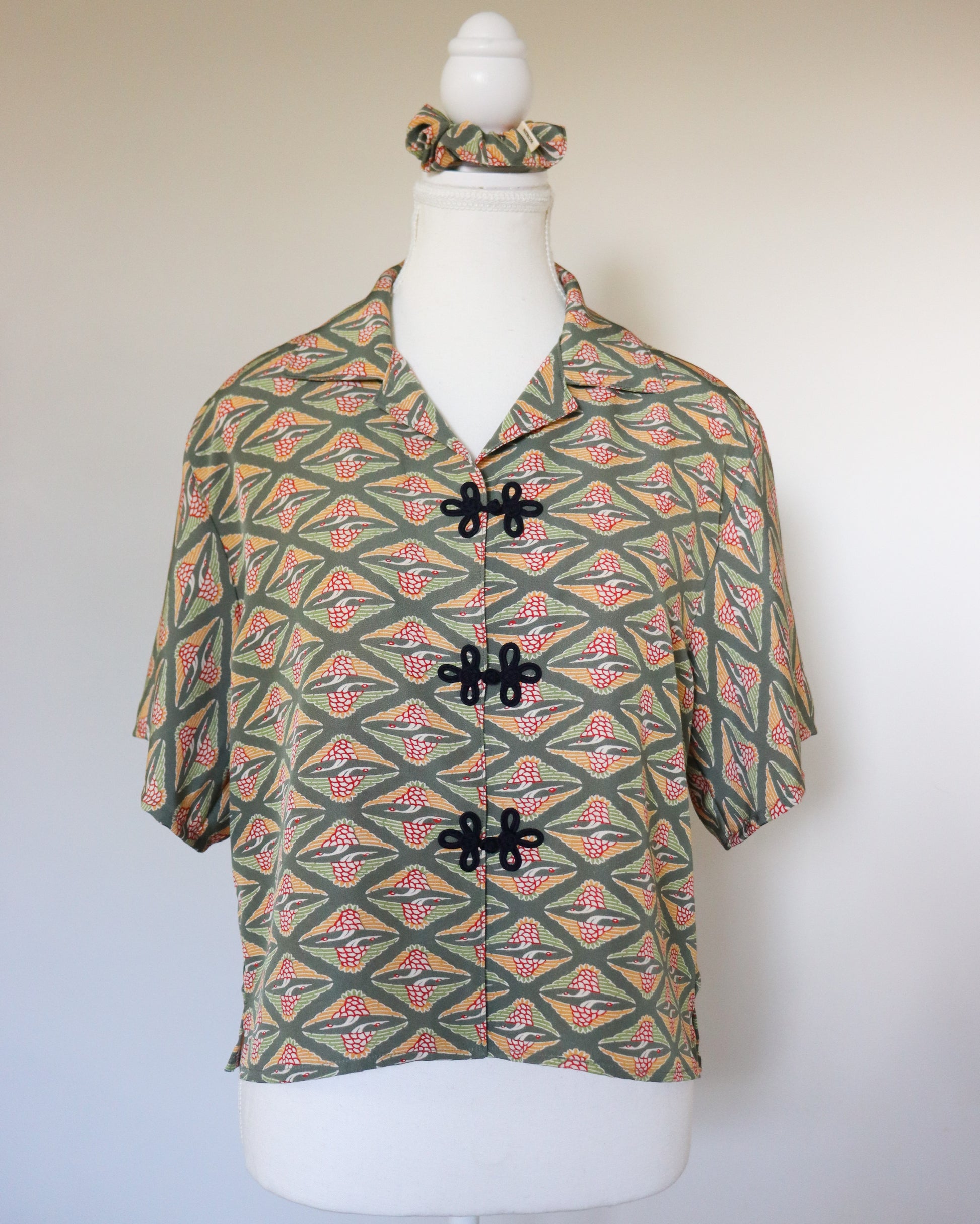 Mannequin wearing a patterned shirt with black buttons on a plain background