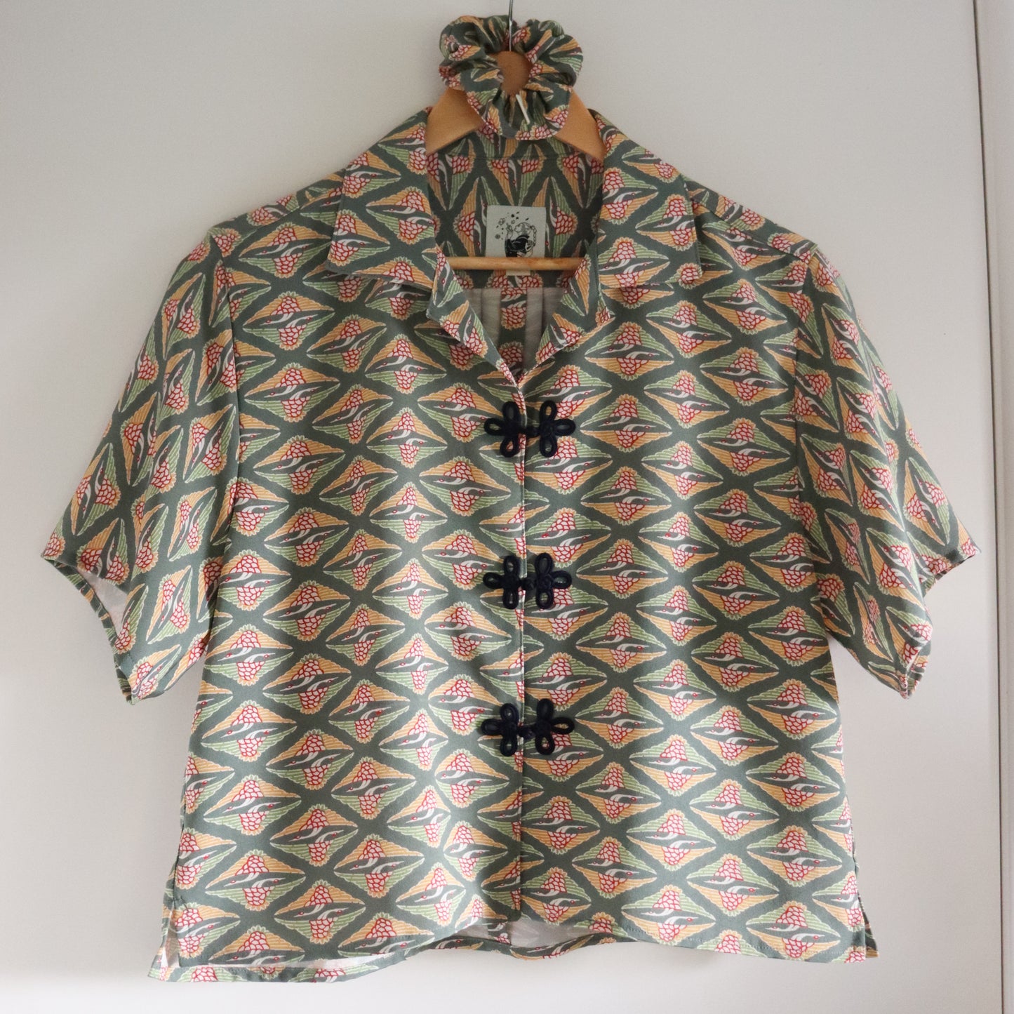Short-sleeve shirt with geometric pattern on a hanger against a white wall
