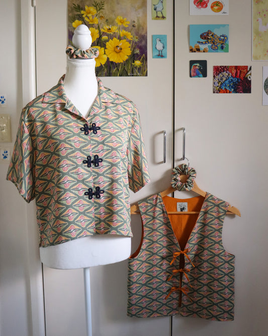Mannequin wearing a patterned shirt with matching vest against a white wall with decorative elements.