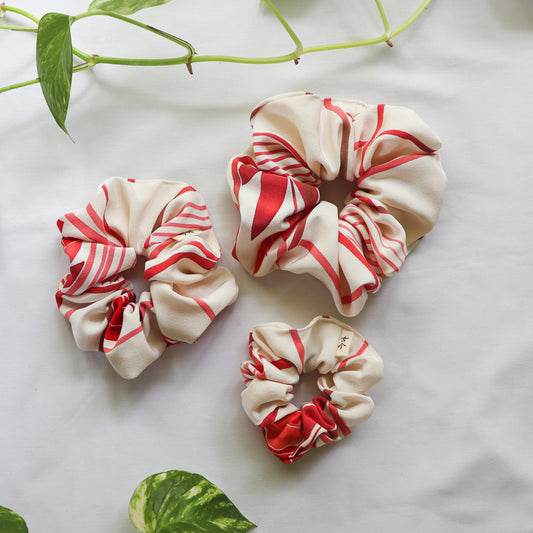 Three red and white striped scrunchies on a light background with green leaves.