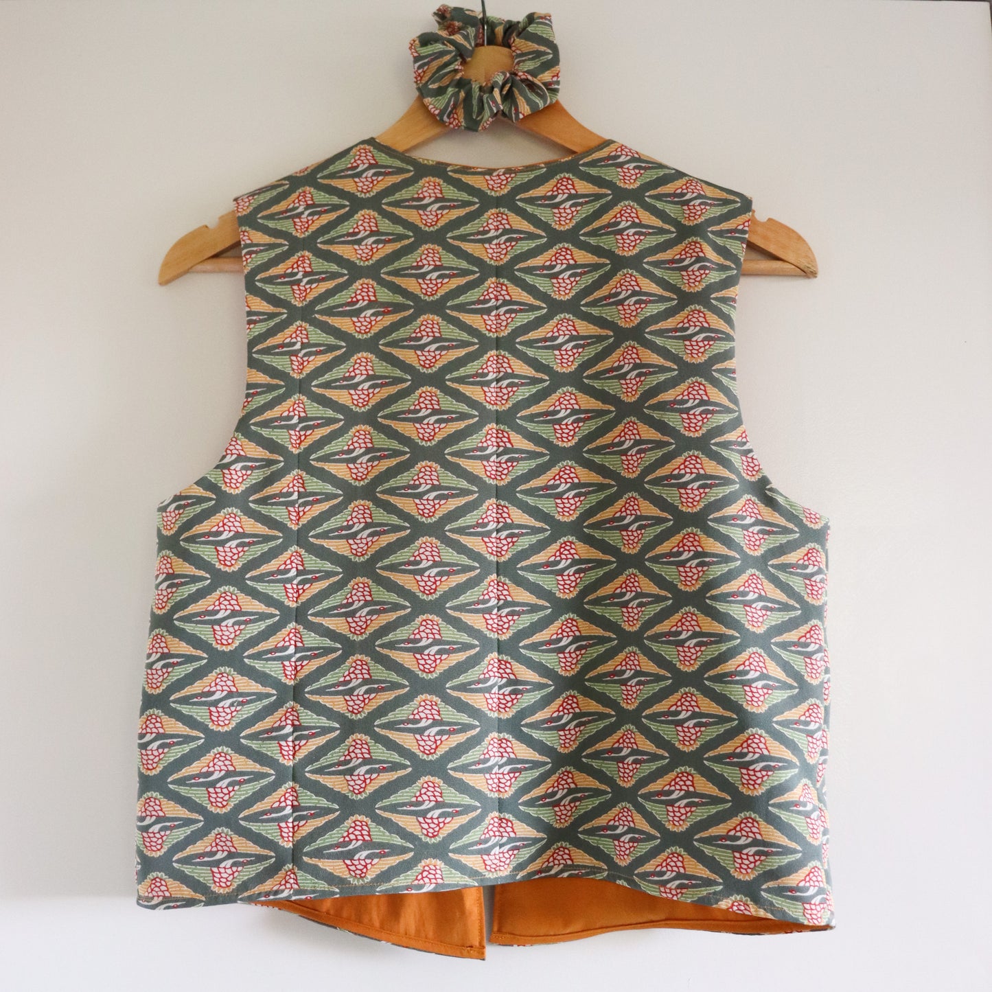 Patterned vest and matching hair tie on a wooden hanger against a white background