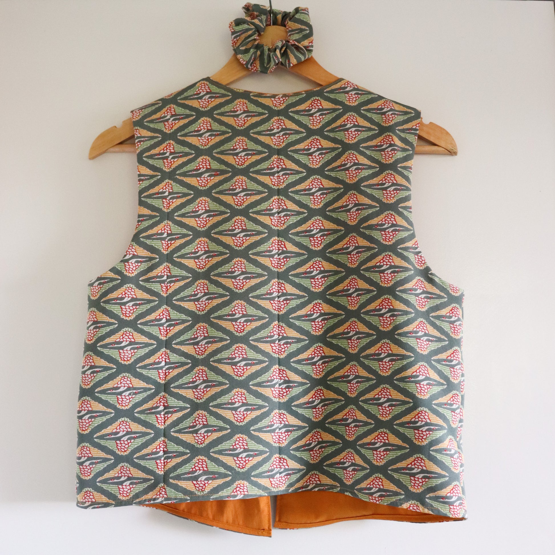 Patterned vest and matching hair tie on a wooden hanger against a white background