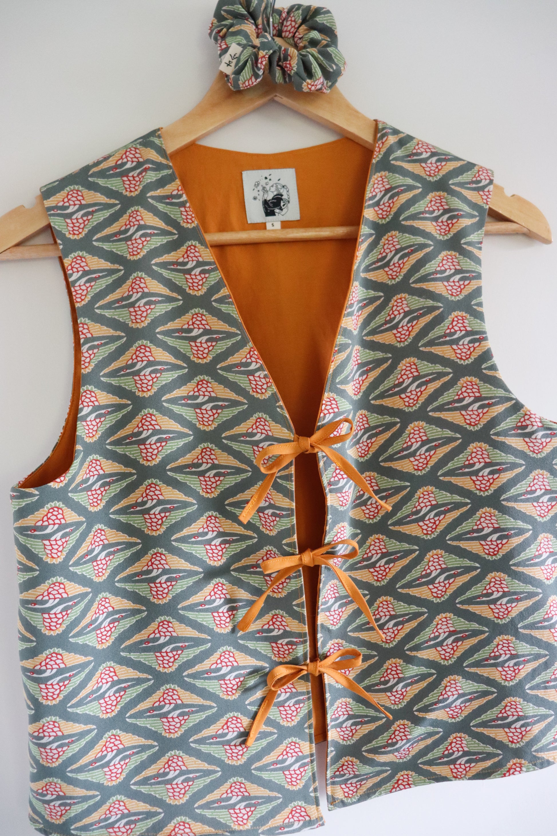 Patterned vest with orange accents on a hanger against a white background