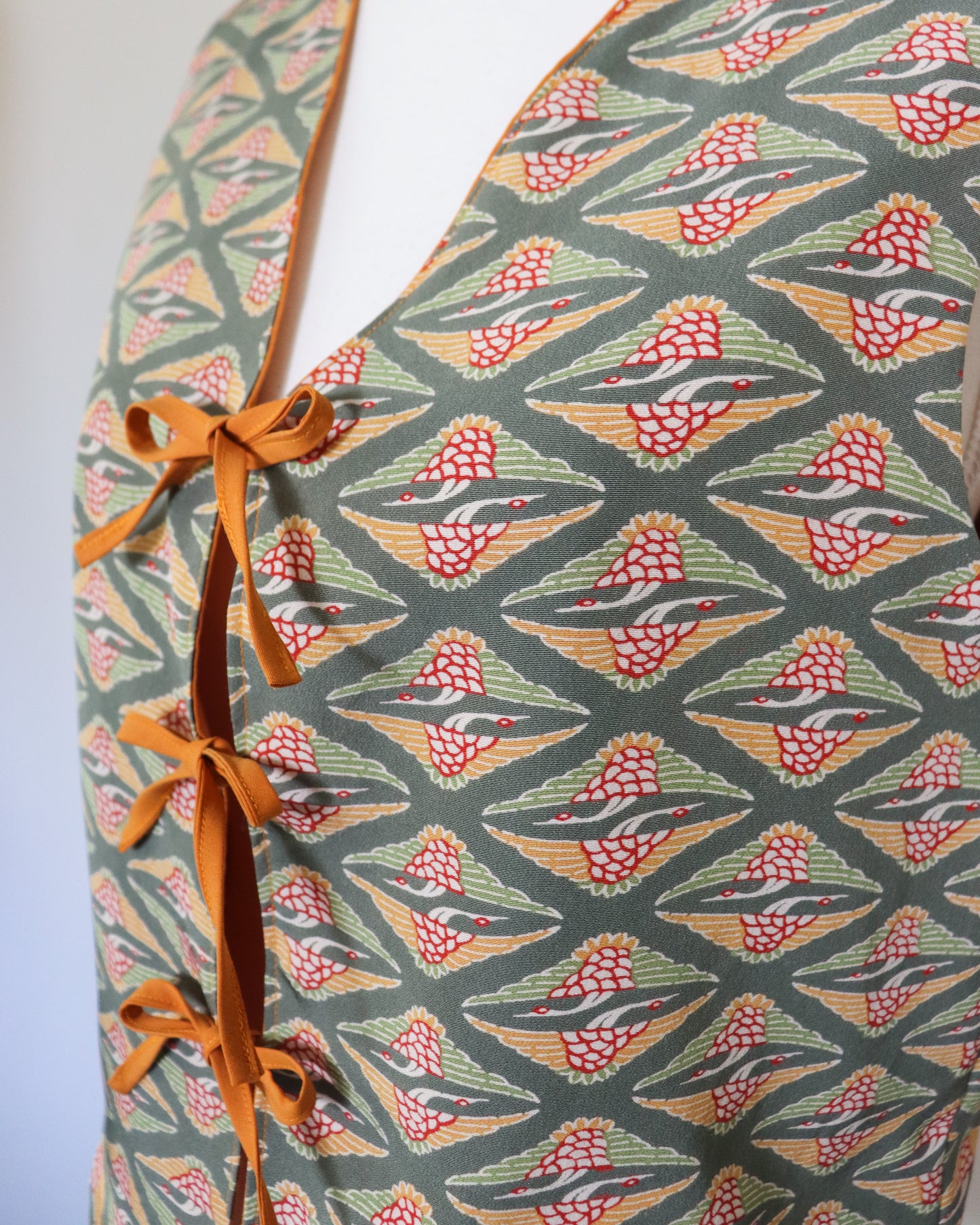 Vest with a geometric pattern featuring birds and orange straps on a plain background