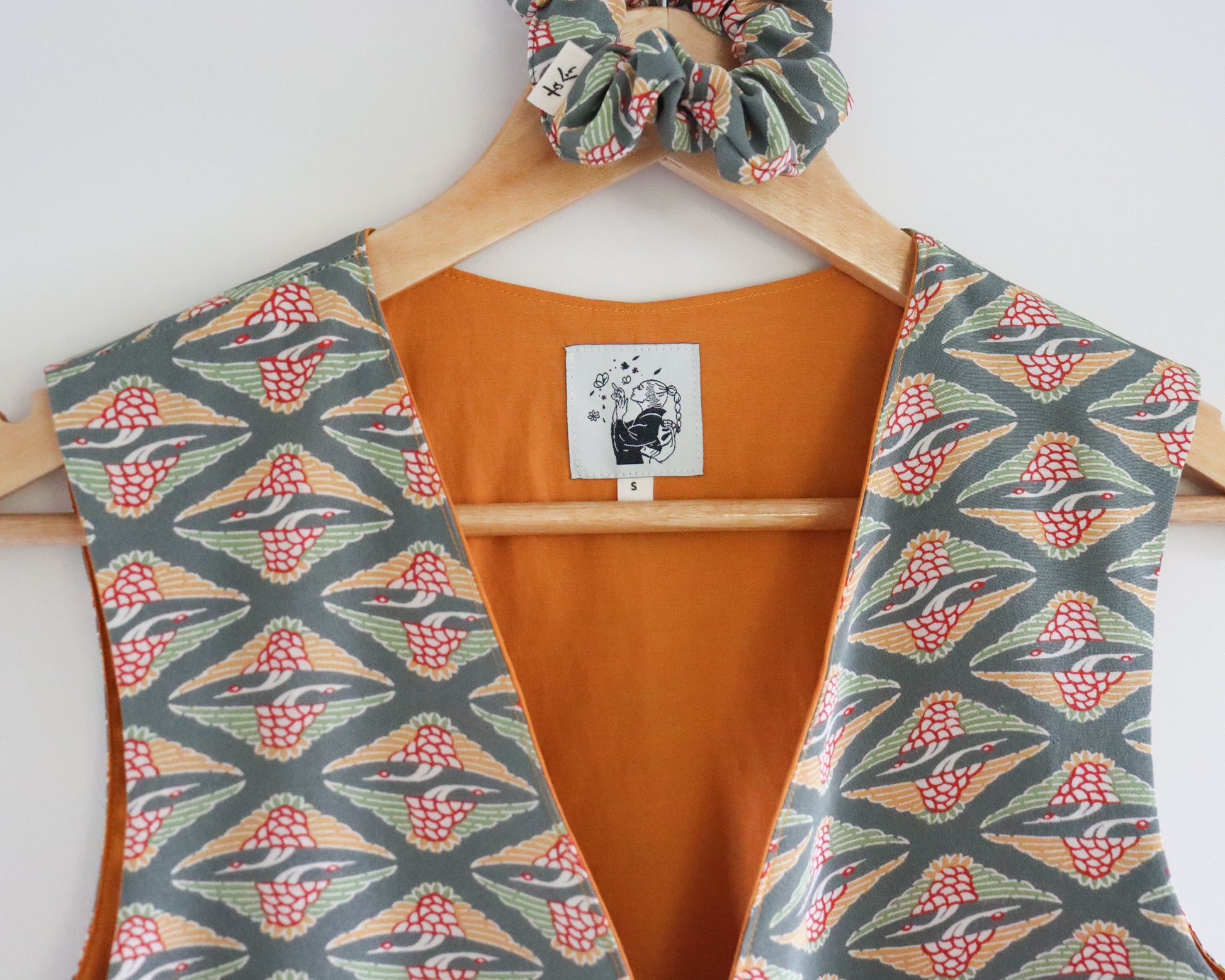 Orange top with a floral patterned vest and scrunchie on a hanger against a white background