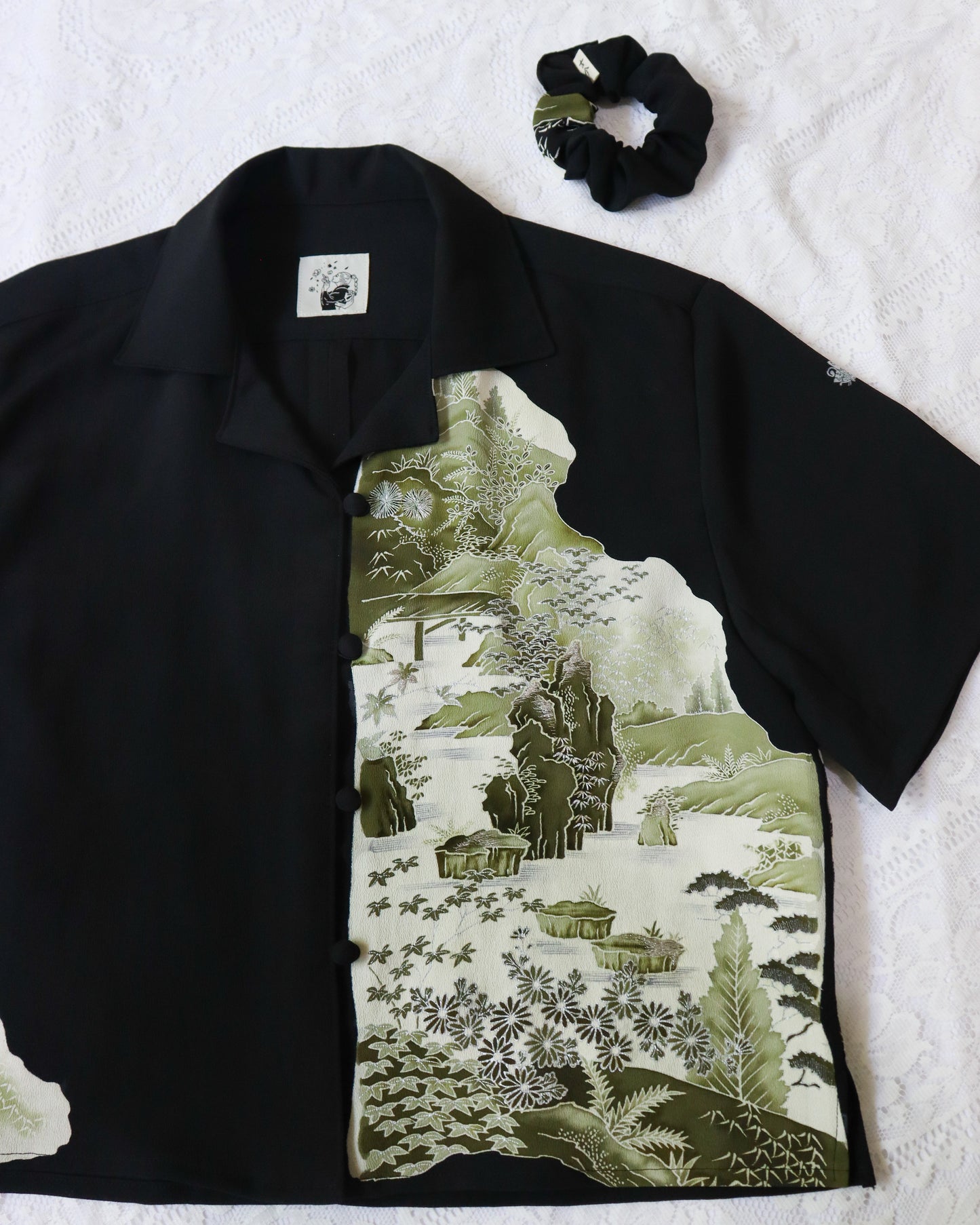 Black shirt with green floral pattern and black scrunchie on white background