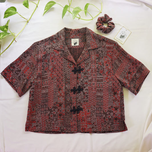 Patterned shirt on a white surface with green leaves in the background